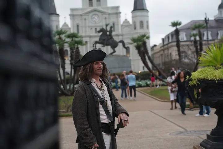 Pirate guide stands in Jackson Square, New Orleans, with tourists in the background.